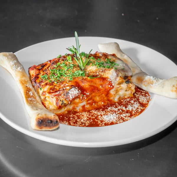 Woodfired lasagna in marinara with breadsticks and fresh herbs.